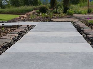Un chemin de jardin en dalles en pierre bleue, gazon et bordures de massif