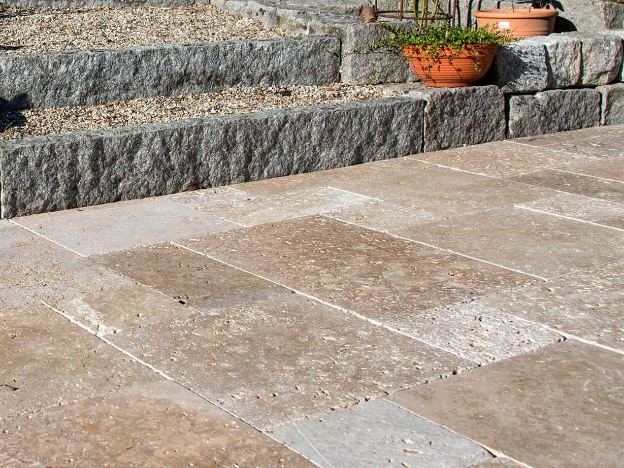 Le travertin Noce se marie parfaitement avec un style maison de campagne Une terrasse avec des dalles de travertin marron et un jardin en arrière-plan.