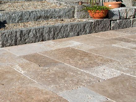 Une terrasse avec des dalles de travertin marron et un jardin en arrière-plan.