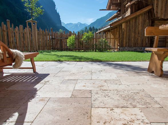Terrasse en travertin Rustic avec meubles rustiques en bois, en arrière-plan une pelouse et une vue sur les montagnes