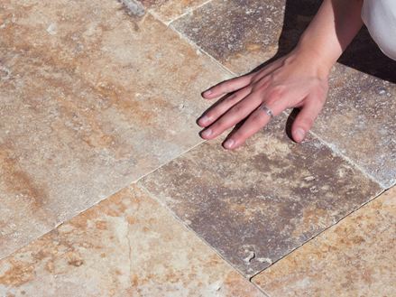 Une main caresse le sol en travertin Scabas