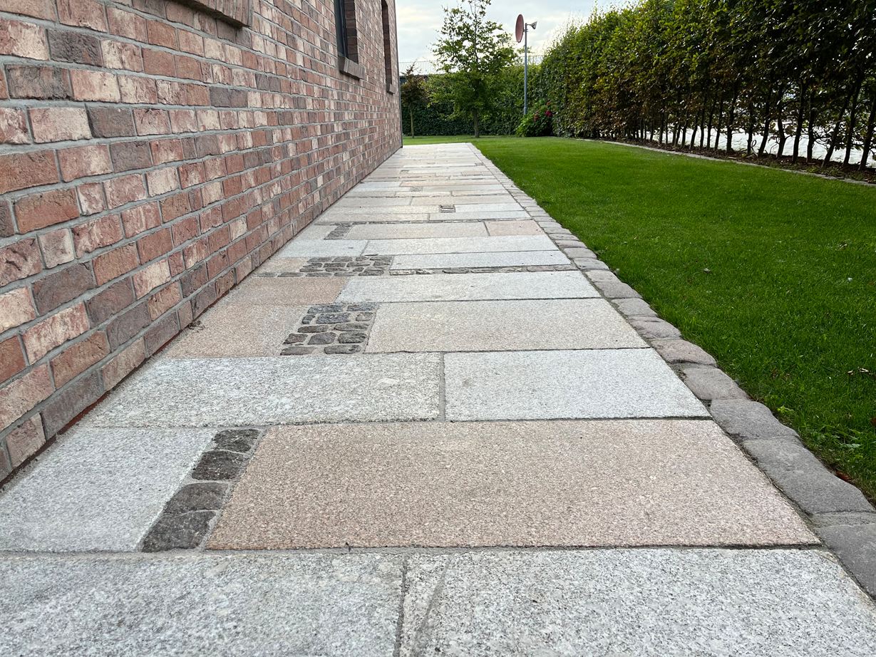 Le jeu de couleurs naturel des dalles en granite Girona Antique est bien visible Girona Antique sur un chemin de jardin contre la maison