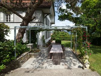 Terrasse Kandla Grey en grès avec un salon de jardin en bois, une fontaine fleurie et de la verdure tout autour