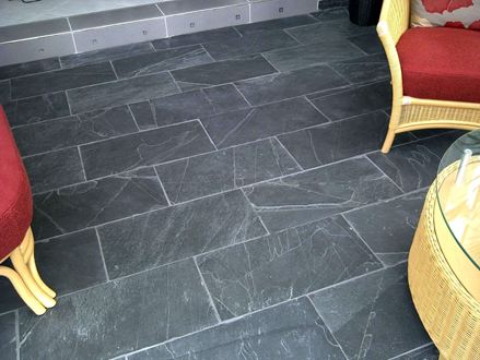 Des meubles rembourrés rouges sur un sol en ardoise noir avec un air rustique. Les joints sont clairs.