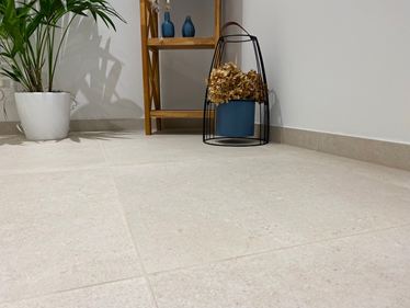 Gros plan sur un carrelage en grès cérame Sevilla Cream imitation pierre calcaire. En arrière-plan, une étagère en bois, une plante et des objets décoratifs.