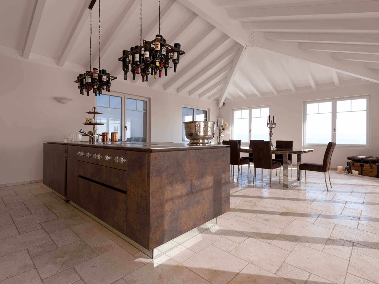 Kücheninsel mit Weinflaschenhalterung an der Decke, im Hintergrund Esstisch und Stühle auf verlegtem Travertin Light mit getrommelter, ungespachtelter Oberfläche Salle à manger lumineuse avec dalles de travertin comme revêtement de sol