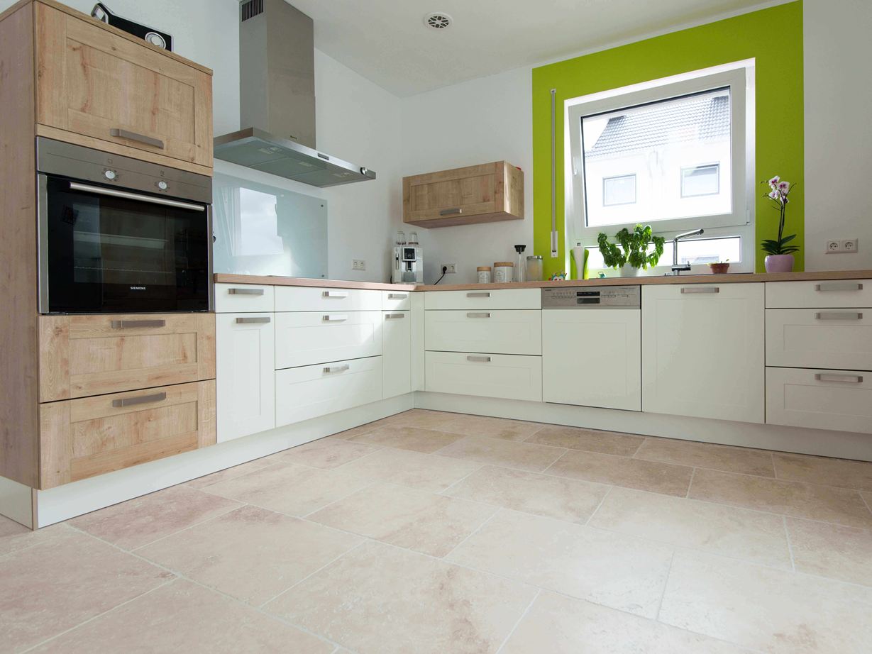 La teinte beige du travertin se marie bien avec le blanc et le bois Cuisine blanche avec éléments en bois et cadre de fenêtre vert sur carrelage en travertin Light tambouriné