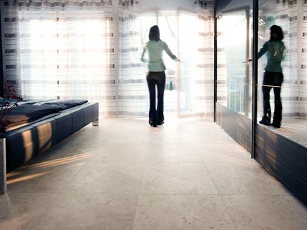 Une femme à la fenêtre d'une chambre dans laquelle on a posé un sol en travertin Medium Line