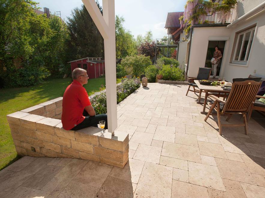 Mann sitzt auf Terrasse mit hellem Travertin im römischen Verband und Natursteinterrasse