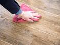 Une main essuie avec un chiffon rose sur des carreaux de grès cérame dans un aspect bois.