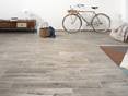 Salon spacieux avec revêtement de sol en grès cérame Urban Smoke, au fond un vélo s'appuie contre le mur blanc.