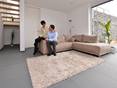 Des carrelages en grand format de l'ardoise Grey Slate dans le salon avec un canapé clair et des murs blancs. Un couple est assi sur le canapé.