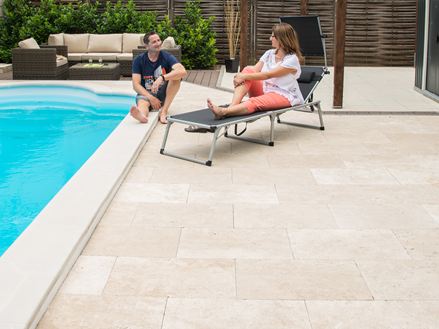 Deux personnes sur une zone avec des plaques de travertin léger au bord d'une piscine moderne.