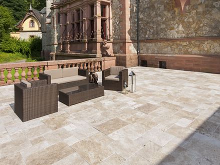 Dalle Medium, en travertin tambouriné. Une terrasse avec des meubles de jardin et un mur en pierre naturelle