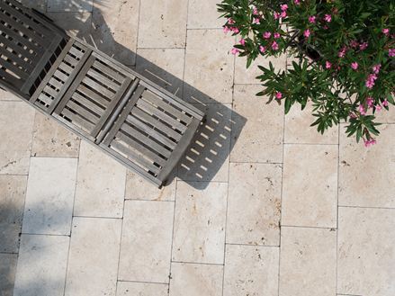 Vue en hauteur d´une chaise longue des dalles de travertin Light et d´une branche sur la droite
