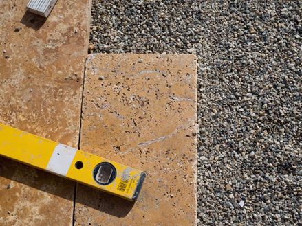 Dalles de travertin dans un lit de gravillons fins, à côté duquel se trouve un niveau à bulle.
