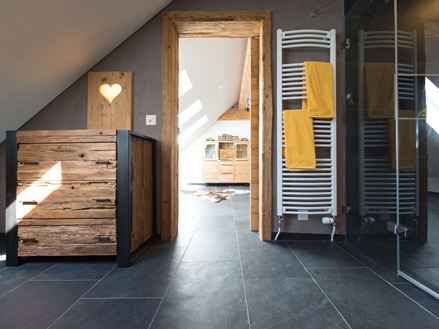 Salle de bain rustique avec meubles en bois, carrelage en pierre naturelle foncée d'ardoise comme revêtement de sol et toit en pente.