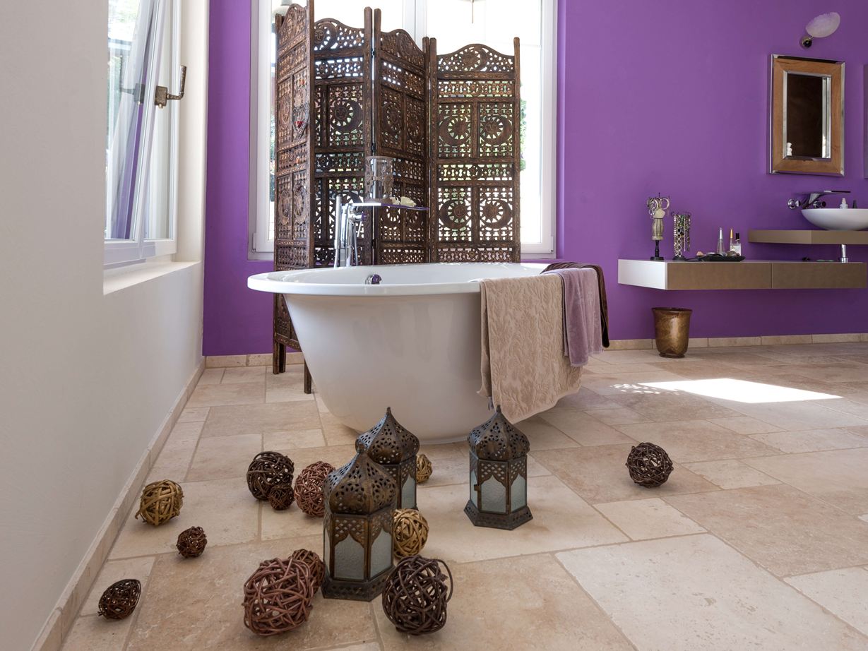 Carreaux de travertin Light dans une salle de bains avec baignoire autoportante et mur violet en arrière-plan