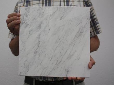 Person hält eine weiße Marmorfliese mit grauen Maserungen in die Kamera