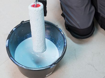 Fliesenleger taucht eine Rolle in einen Eimer mit Grundiermittel