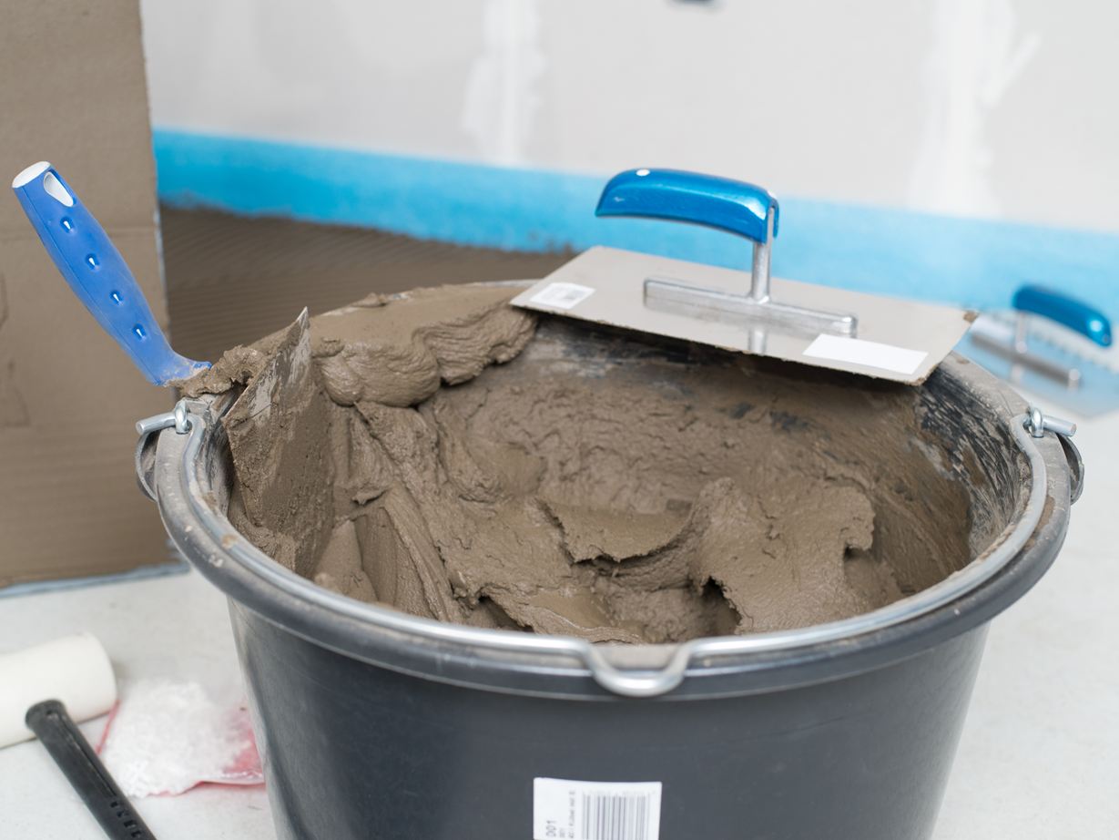 Un seau avec de la colle pour pierres naturelles et une truelle à dents