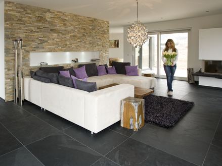 Modernes Wohnzimmer mit Natursteinverblender an der Wand, Schieferfliesen als Bodenbelag und einer weißen Couch