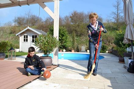 Une femme balaye la terrasse avec des dalles de pierre naturelle pendant que l'enfant joue