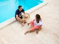 Homme et femme assis à la piscine, sol en travertin, carreaux de terrasse