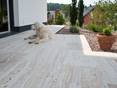Un chien s'allonge sur une terrasse avec des plaques de travertin Natura